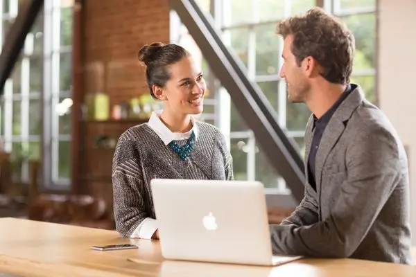 Homme et femme discutant devant un Mac portable