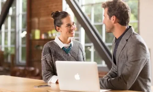 Homme et femme discutant devant un Mac portable